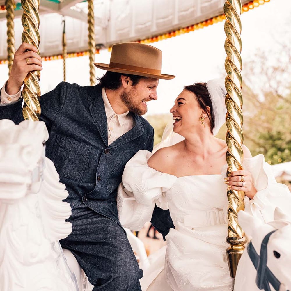 The bride in a statement gown and groom in double denim ride on the carousel together 