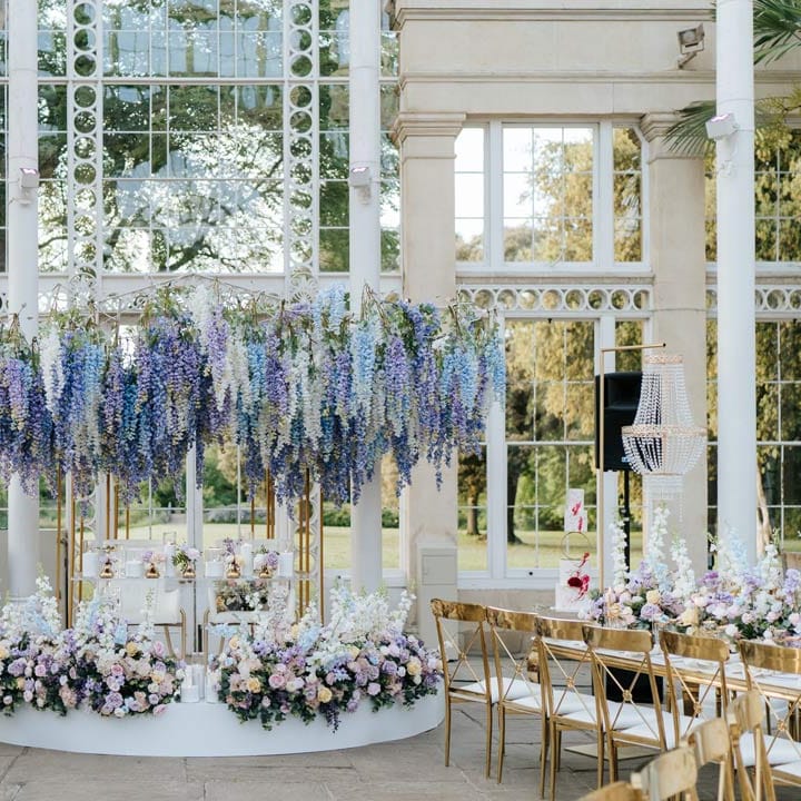 Syon Park wedding venue reception room with gold chairs, botanical tablescapes with large pastel flower centrepieces and suspended pastel foliage decor 
