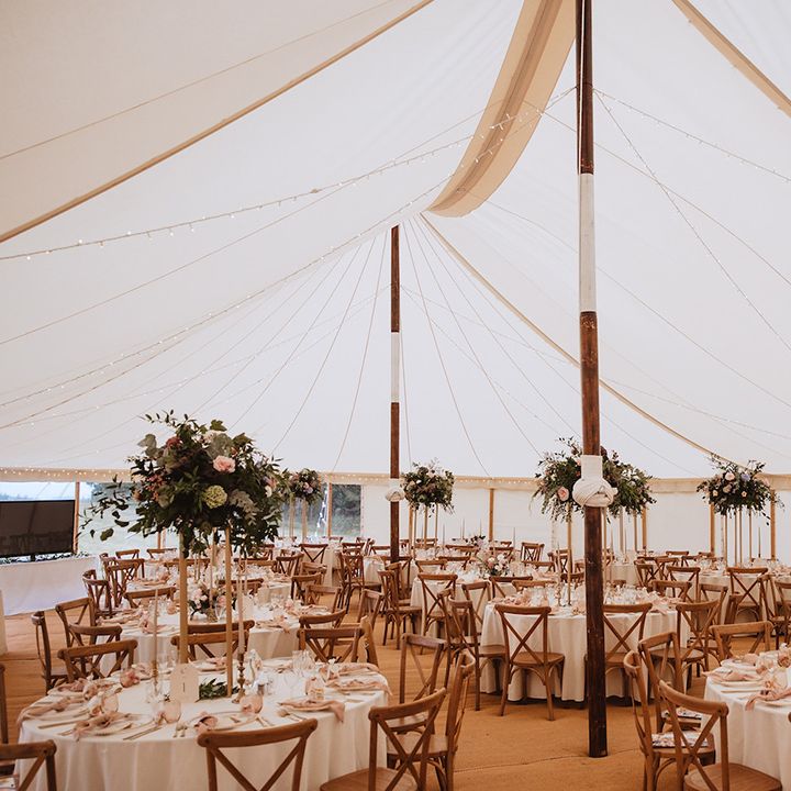Round tables decorated with tall floral centrepieces at marquee wedding reception 