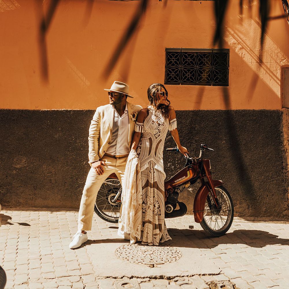 The bride and groom pose in their boho outfits on a motorbike 