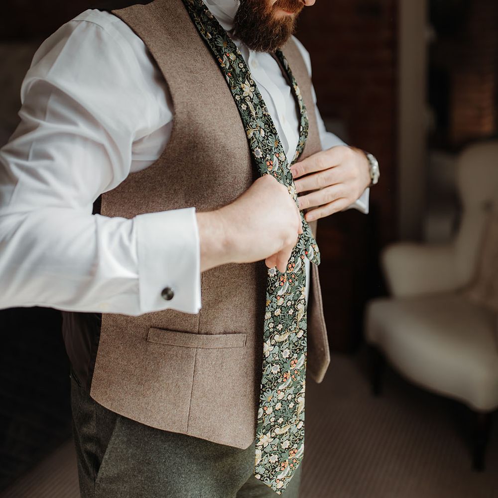 Groom wearing floral patterned tie with light brown waistcoat getting ready for the wedding 
