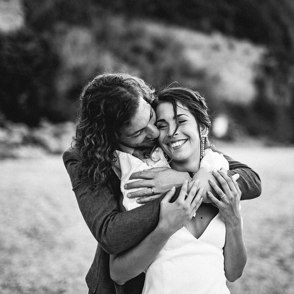 Groom with curly hair embracing his bride in a ruffle sleeve wedding dress on the beach in Italy 