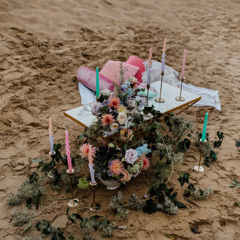 Intimate picnic table on the beach with pastel coloured flowers, cushions and candles styled by Pink Palms 