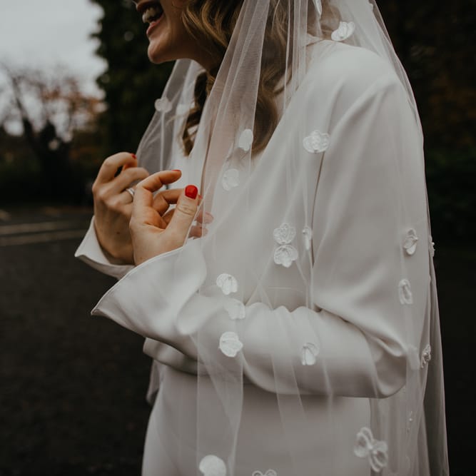 Bride with bright red nail polish holding her appliqué wedding veil 