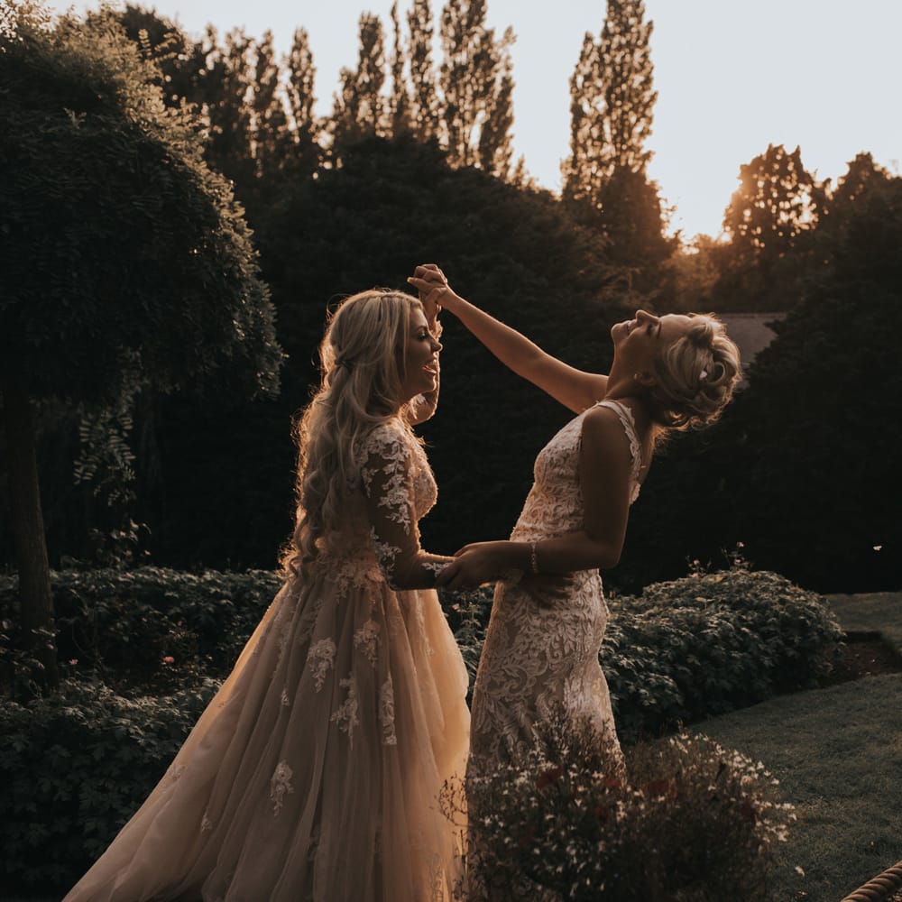 Two brides dance outside at sunset.