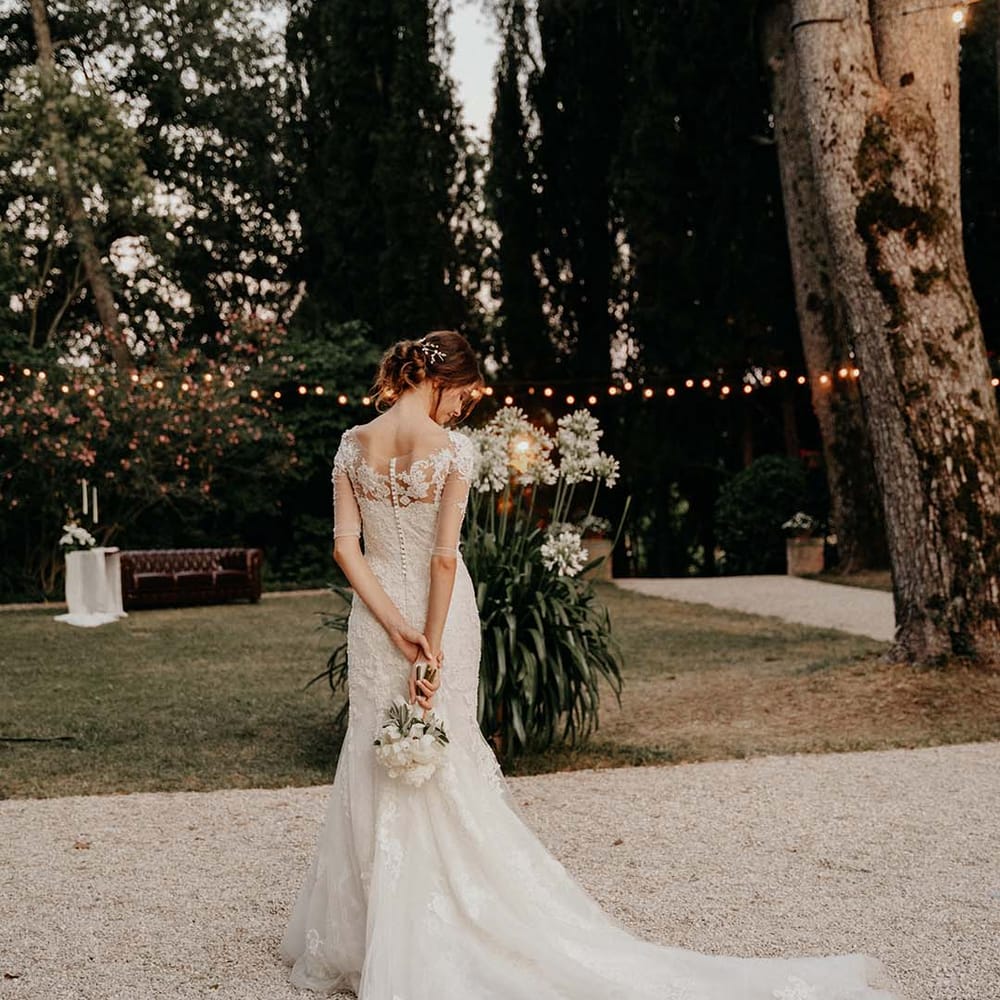 Bride looks down as she wears lace wedding gown and holds her floral bouquet behind her | Royal Studio