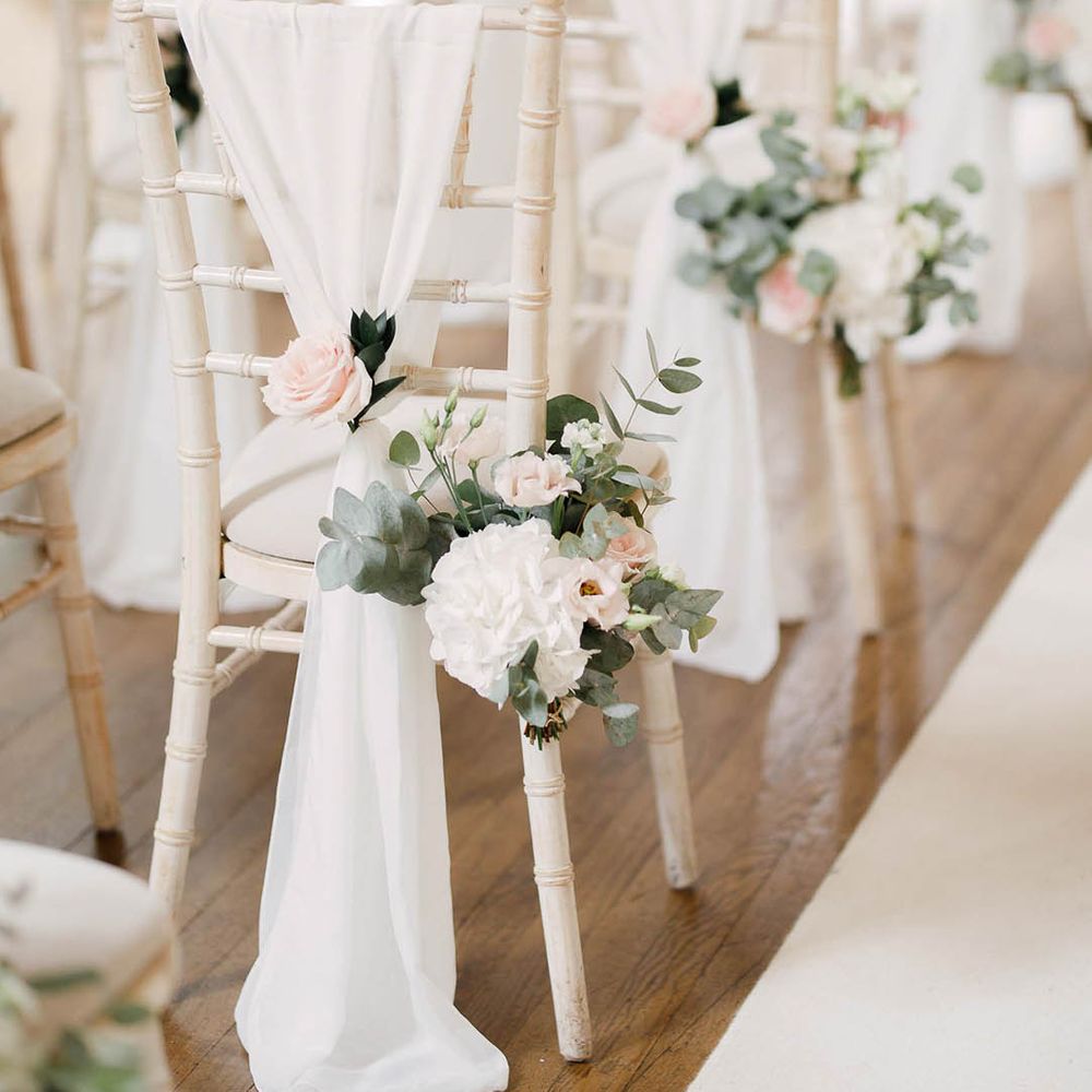 White wicker chairs complete with white fabric draped across and florals tied to the back