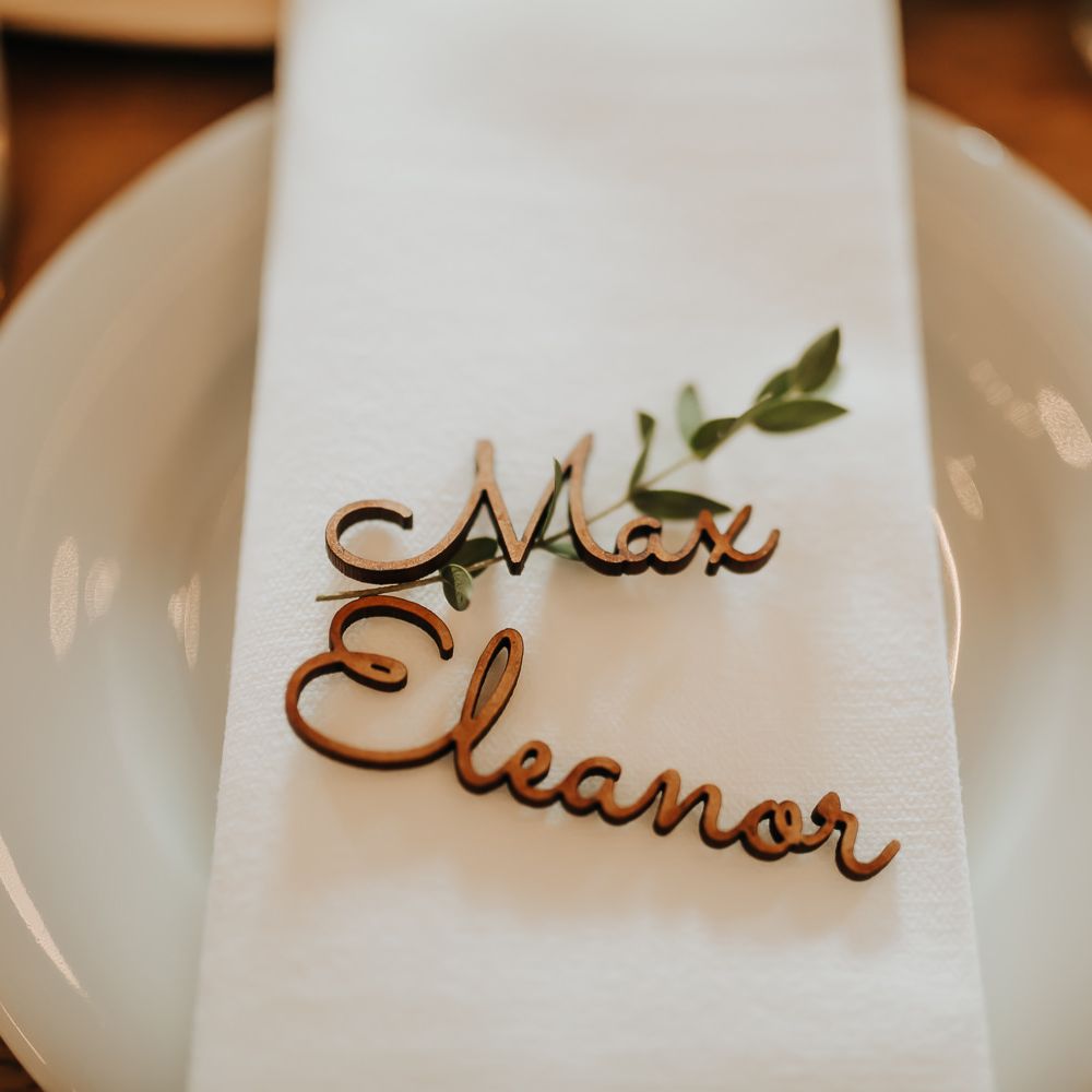 Wooden personalised table place names on white napkin with foliage stalk for rustic wedding decor 