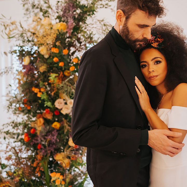Black bride with afro hair in an off the shoulder wedding dress laying on her grooms chest in a black suit and top