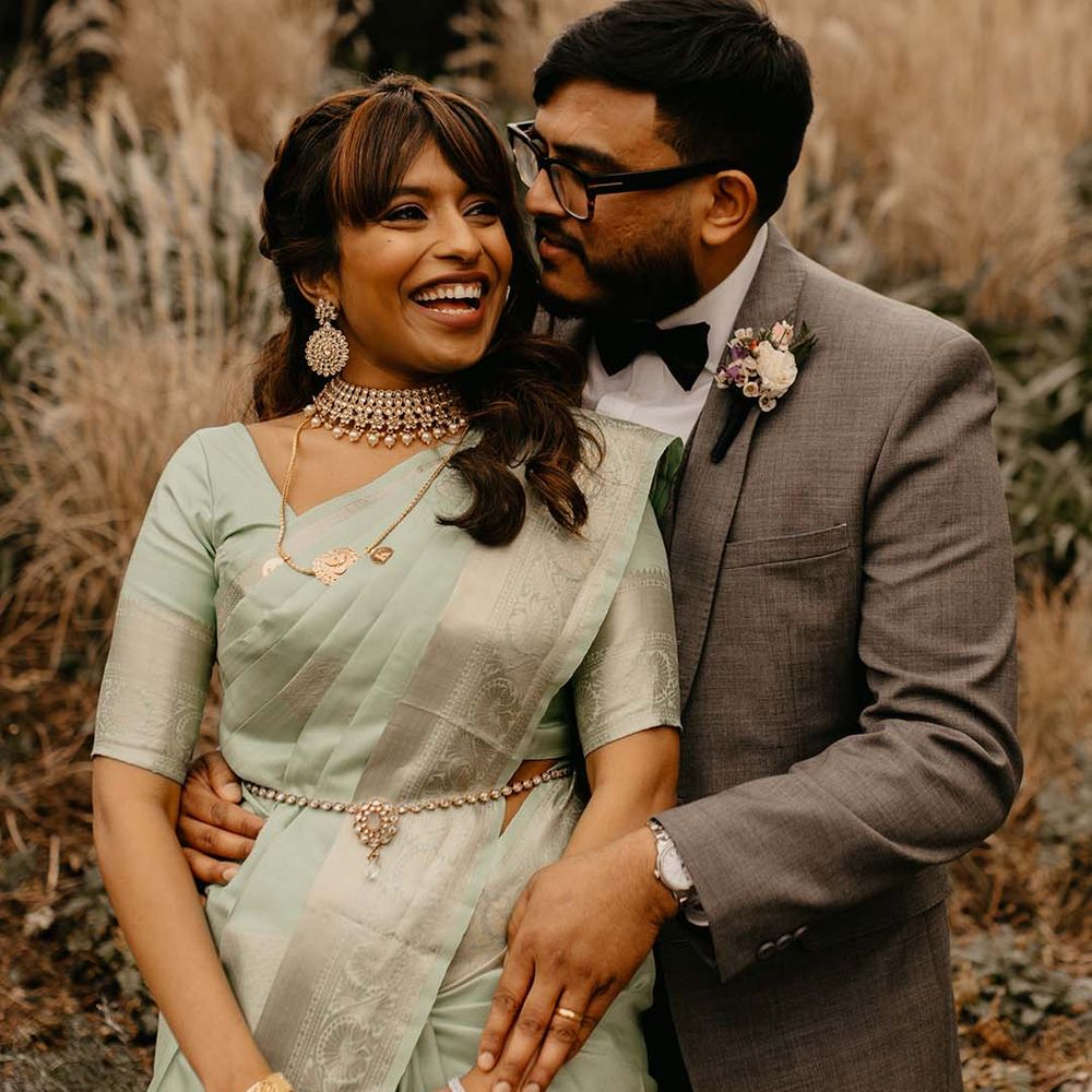Bride in mint green saree and groom in grey suit embracing and smiling at multicultural wedding