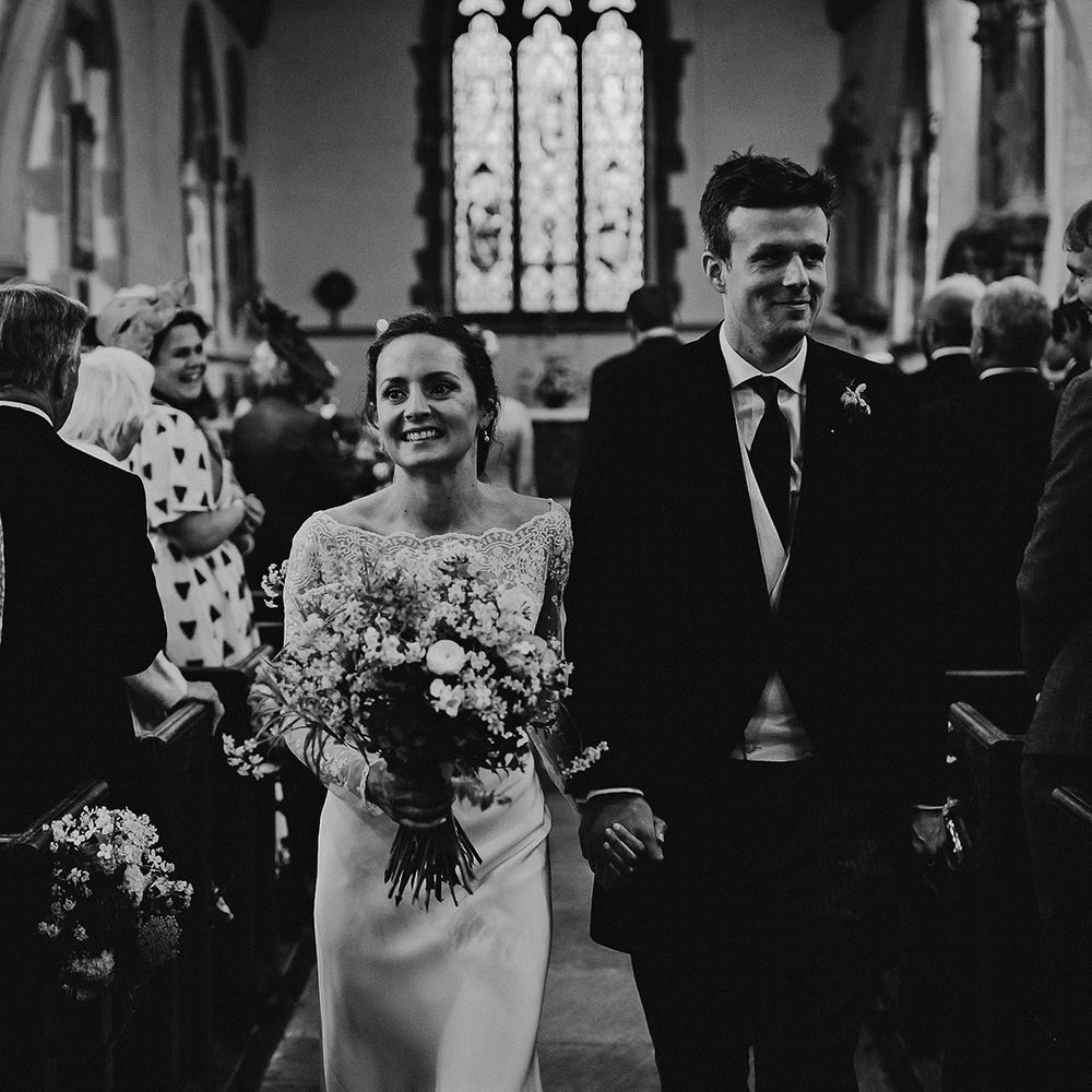 Bride in satin wedding dress walks back down the aisle with the groom as a married couple after church ceremony