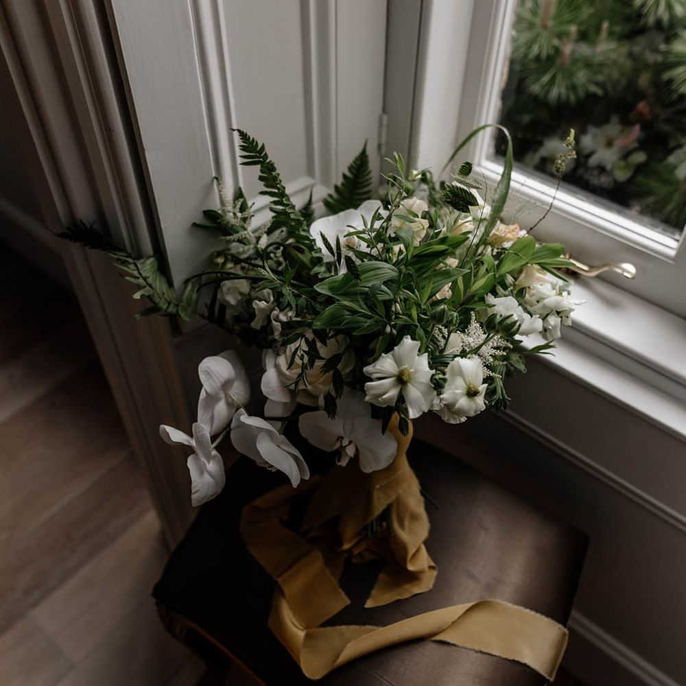 White and green wedding bouquet tied with ribbon resting on a window ledge 
