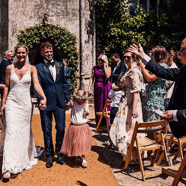 Bride and groom walk with their daughter through confetti as they have confetti exit from outdoor wedding ceremony 