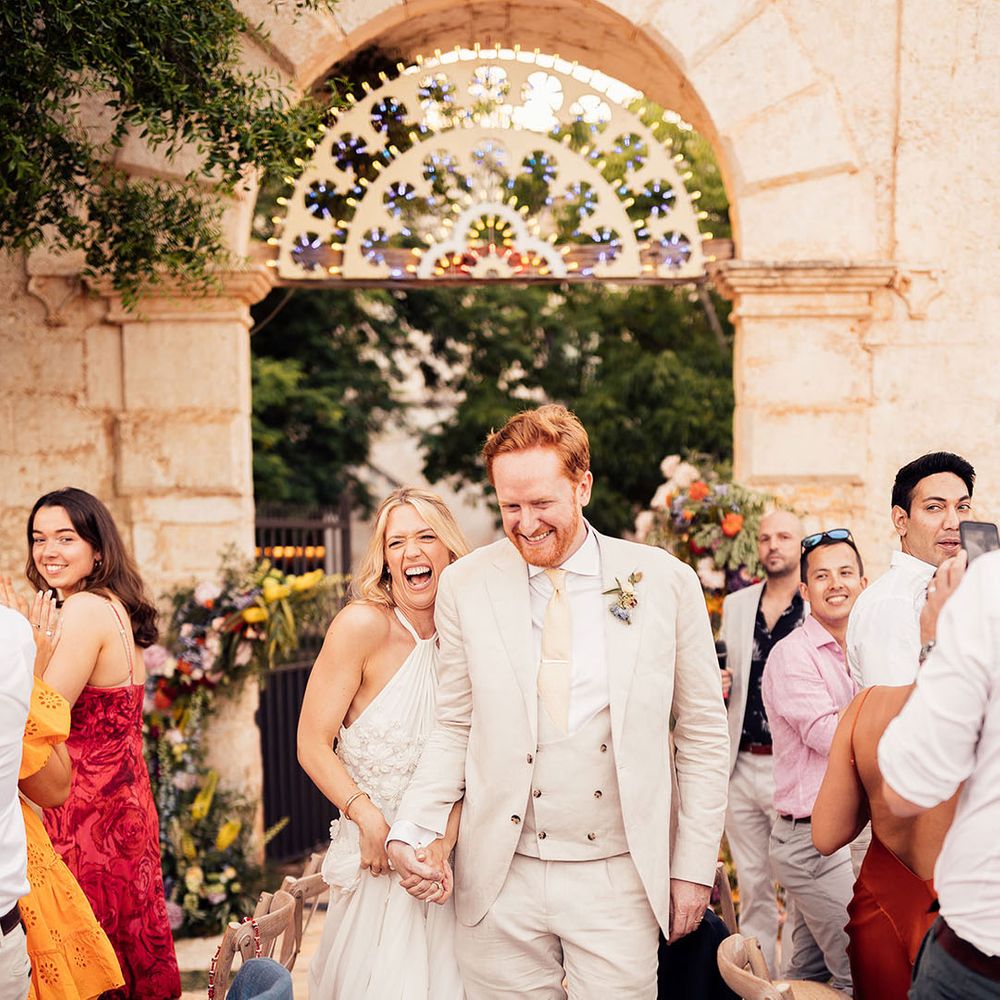 Bride and groom enter their outdoor wedding reception with the wedding guests applauding on their feet