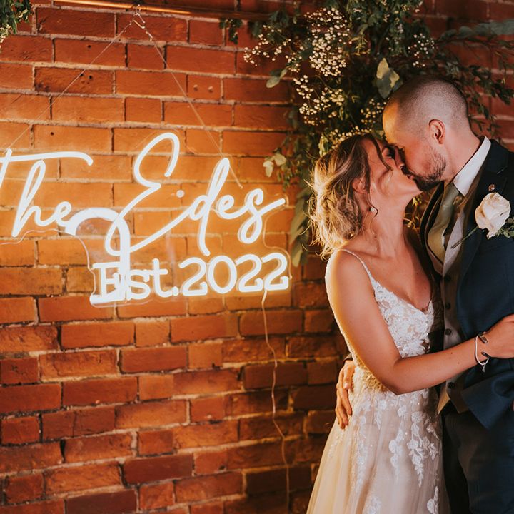 Bride and groom share an intimate kiss next to their custom white neon wedding sign