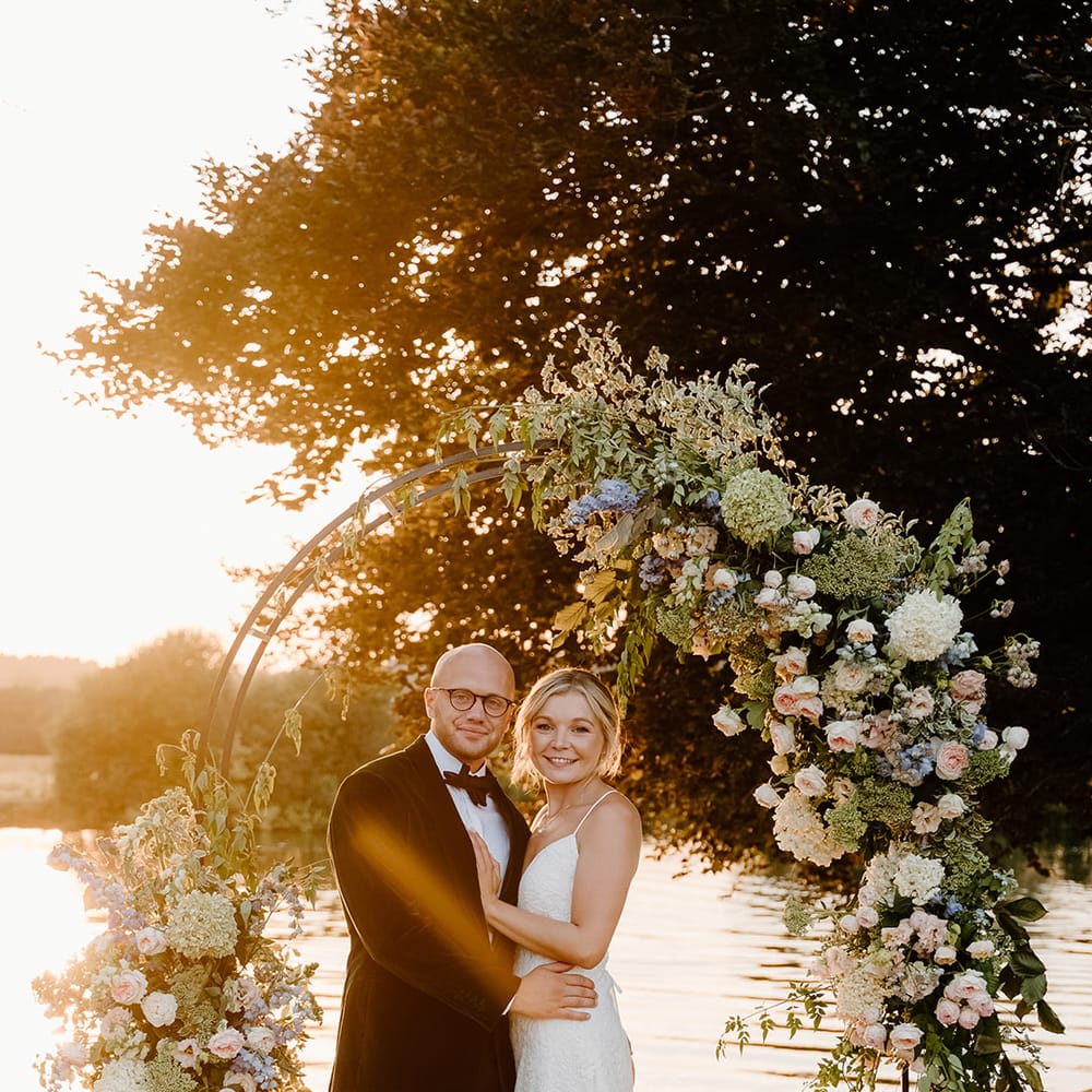 Bride & groom stand beneath steel floral archway during golden hour