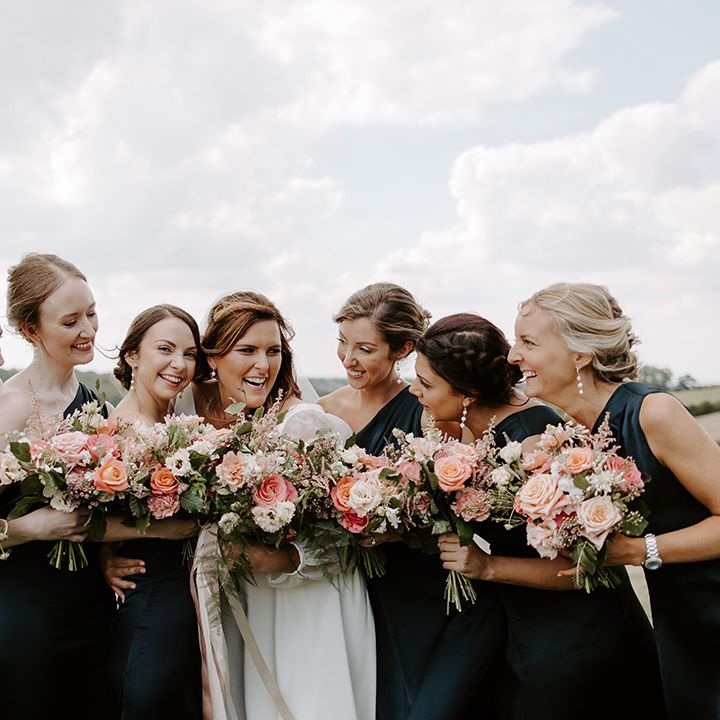 Bride stands with her bridesmaids in deep blue satin bridesmaid dresses whilst holding colourful floral bouquets 