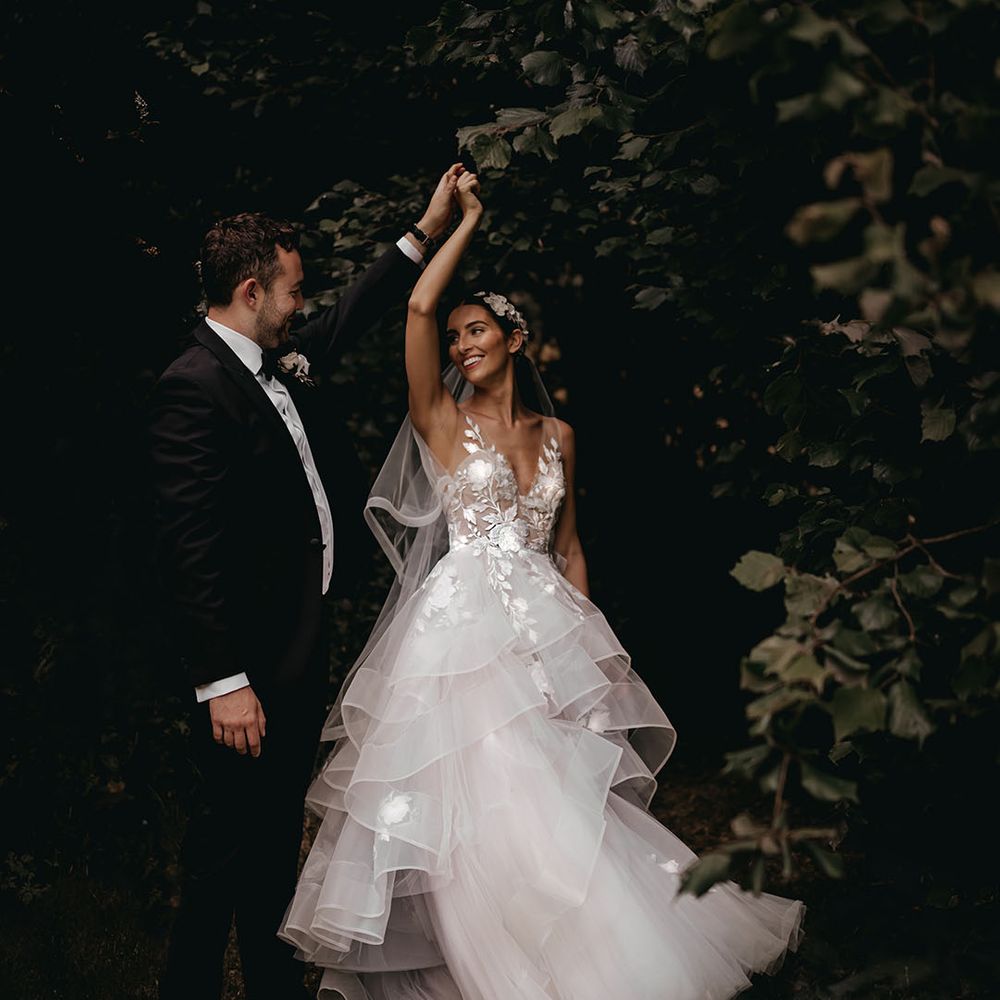 Groom in a black tuxedo spins the bride around in a pretty flower tulle wedding dress