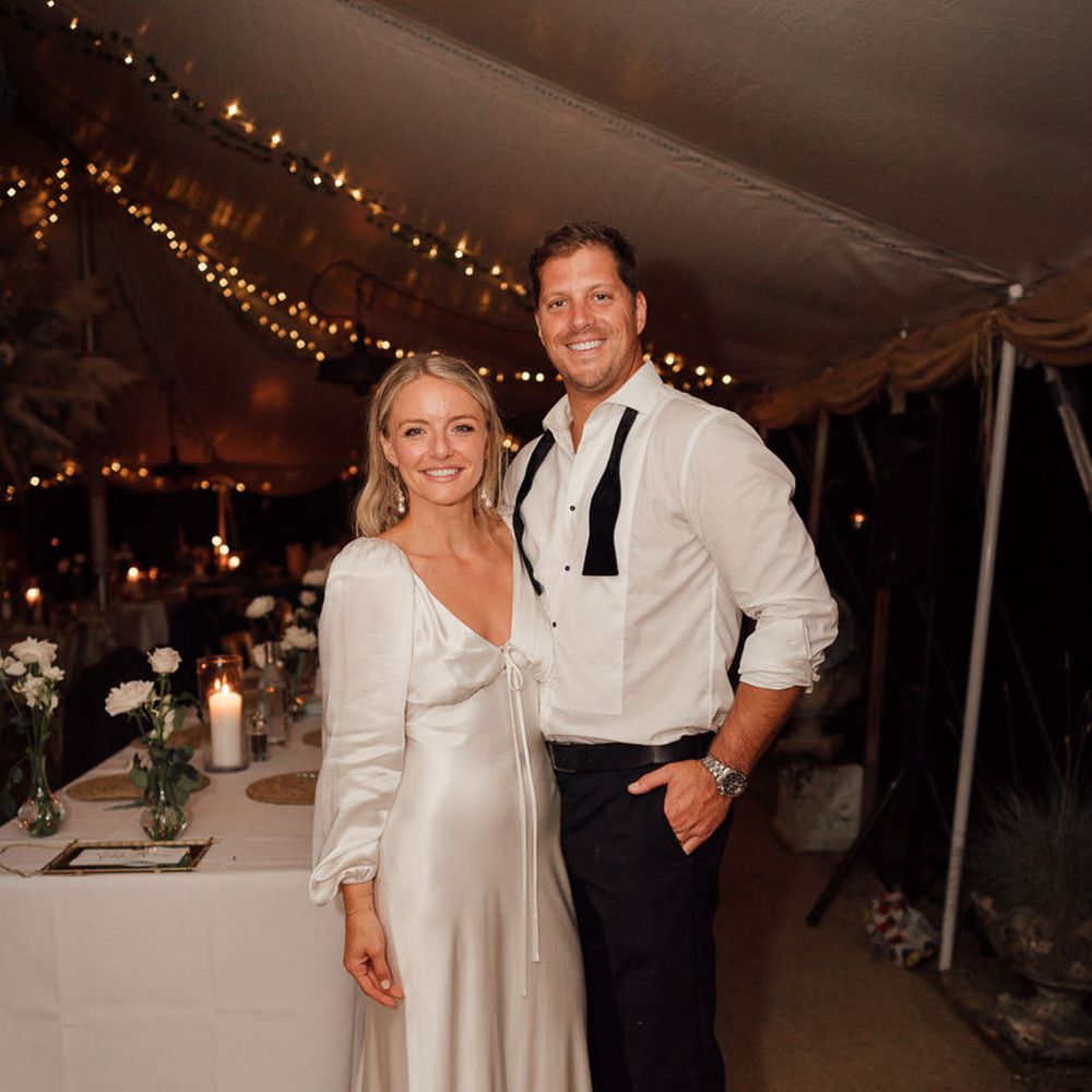 Bride in second white dress for the evening posing and smiling with the groom in a white shirt and undone bow tie 