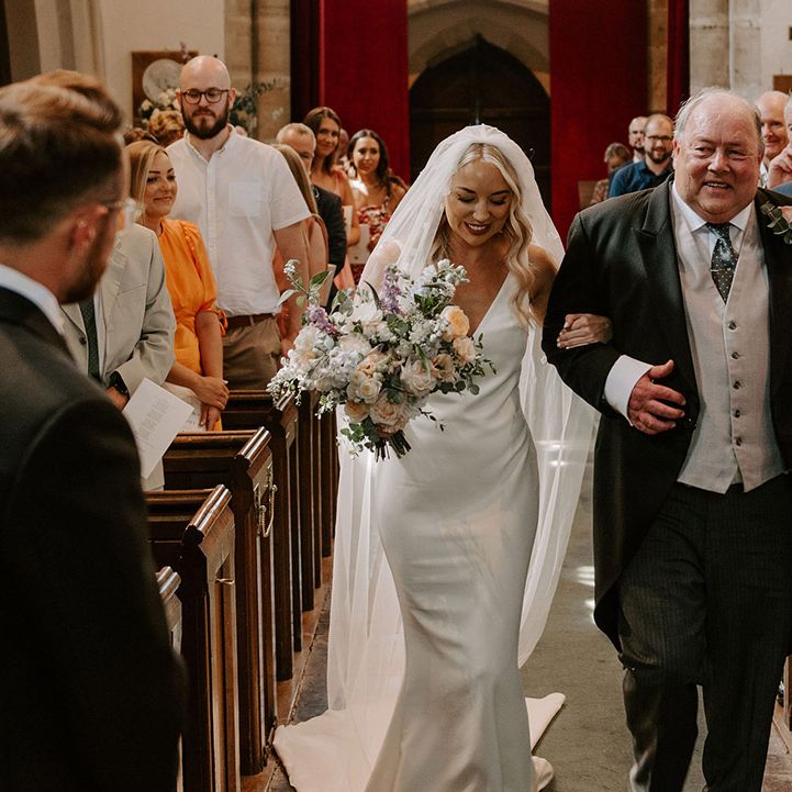 Father of the bride in a three piece suit walks down the aisle with the bride to meet the groom at the altar 