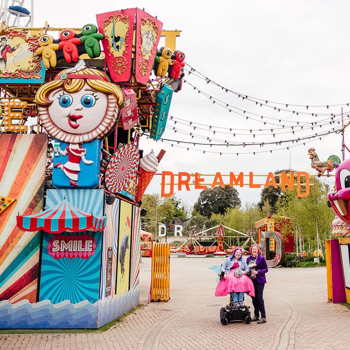 Brides standing outside Margate Dreamland theme park wedding with large colourful rides, signs and fairy lights hanging above 