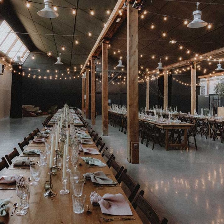 Wooden banquet tables in industrial setting complete with festoon lighting 