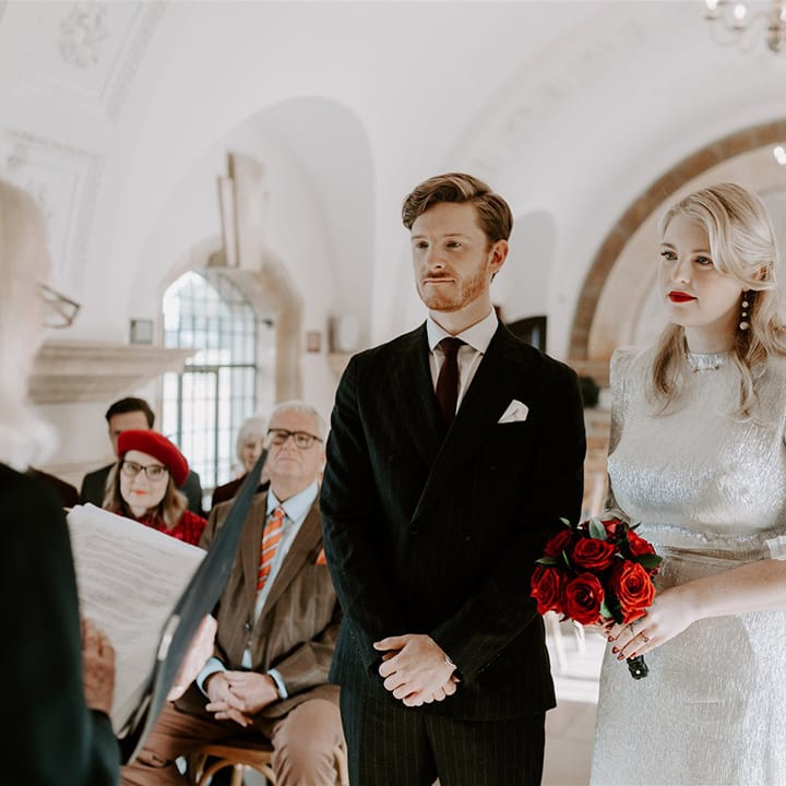 Elopement style wedding planned in six months with the bride holding a small round red rose bouquet with red lipstick 