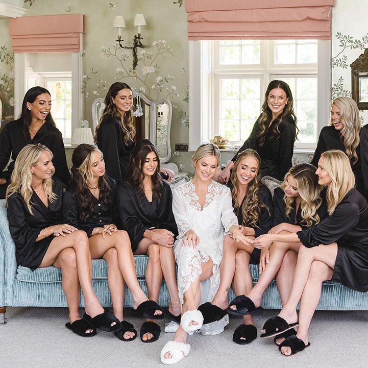 Bridesmaids in matching black satin bridesmaid robes and slippers with the bride as they get ready for the wedding 