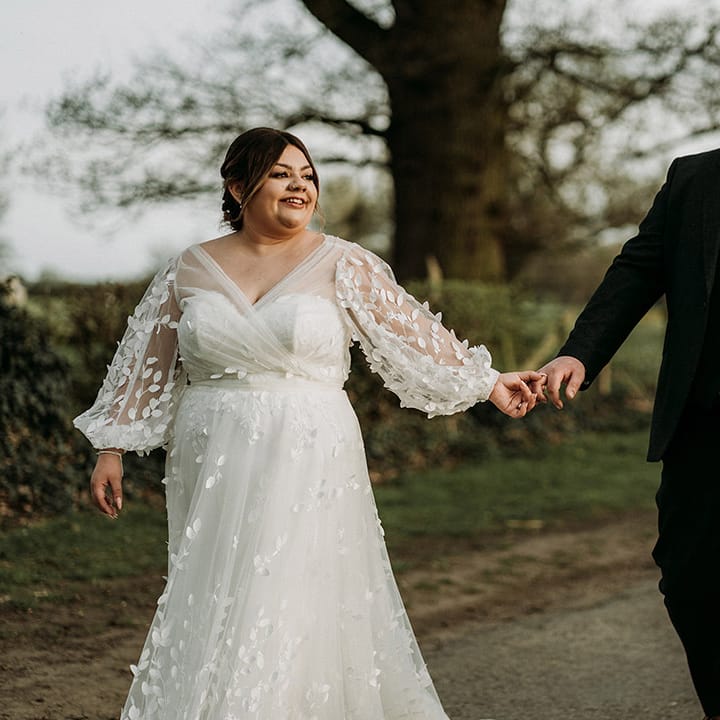 Groom in three piece green tweed wedding suit walking hand in hand with the bride in a long sleeve wedding dress 
