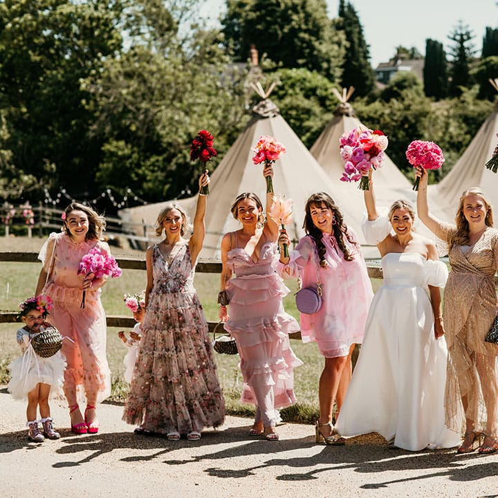Bridesmaids in pink mismatched bridesmaid dresses with pink bouquets standing with the bride in front of the tipi wedding 