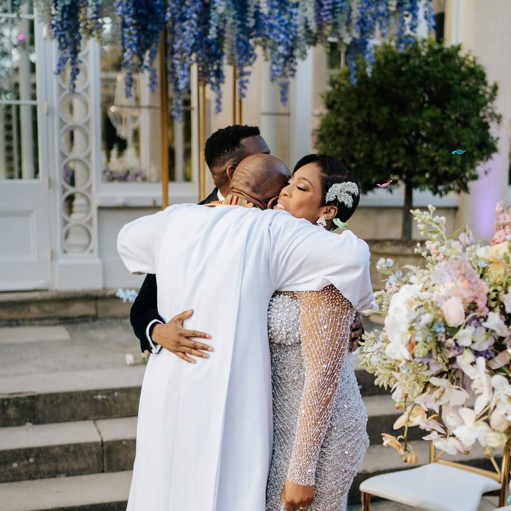 Bride in illusion v neck sheer off shoulder long sleeve pearl embellished wedding gown being hugged by groom and officiant at Syon Park vow renewal