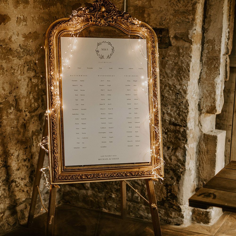 Gold wedding table plan decorated with fairy lights for cosy rustic barn wedding in Yorkshire countryside 