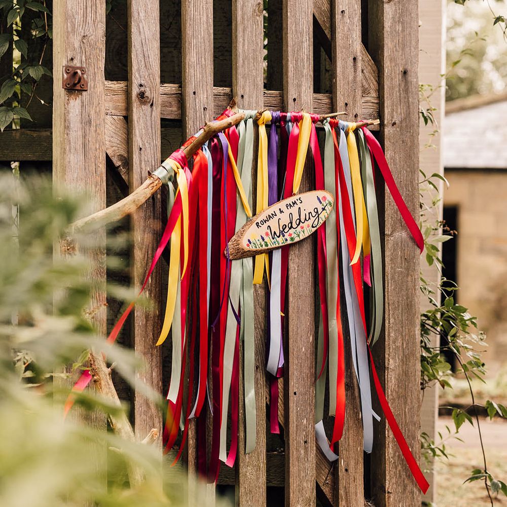Rainbow coloured ribbons hang with DIY wood slice wedding sign 