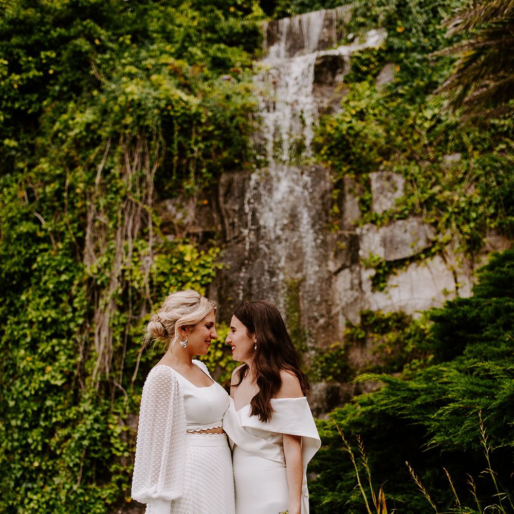 Couple portrait of two brides wearing white wedding gown and two piece with pastel bouquet
