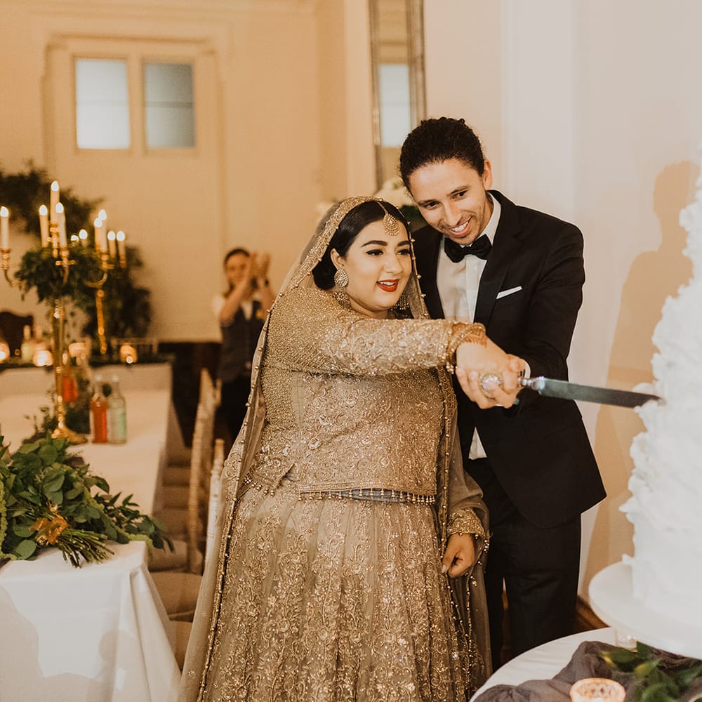 Bride in a  gold wedding dress and groom in a tuxedo cutting the wedding cake 