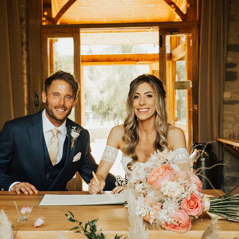 Groom in navy suit and boho bride sign wedding register at Tythe Barn wedding