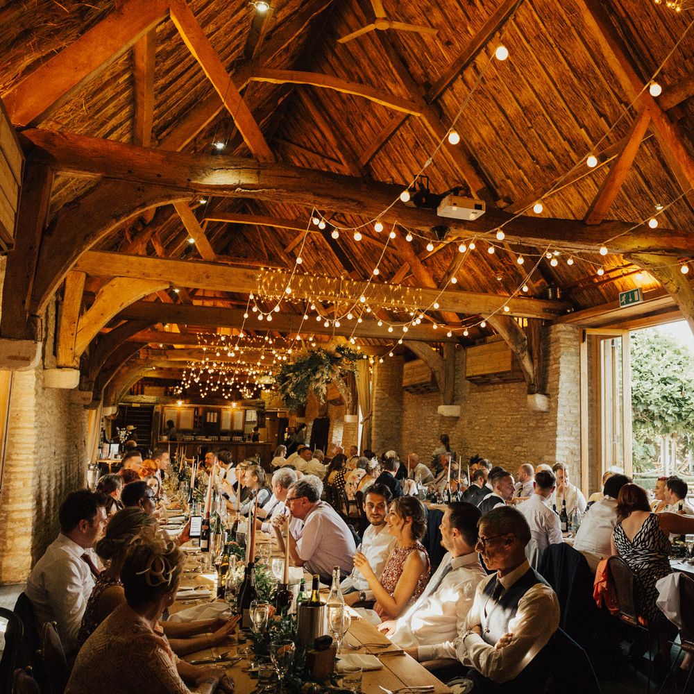 Guests enjoy meal inside barn at Tythe Barn Wedding with boho decor