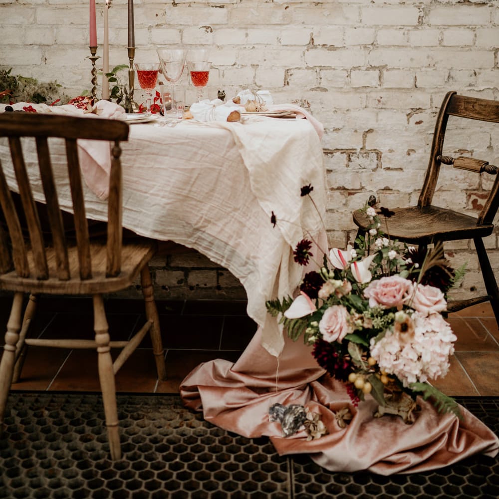 Sweetheart table next to an exposed brick wall dressed with taper candles and natural linens 