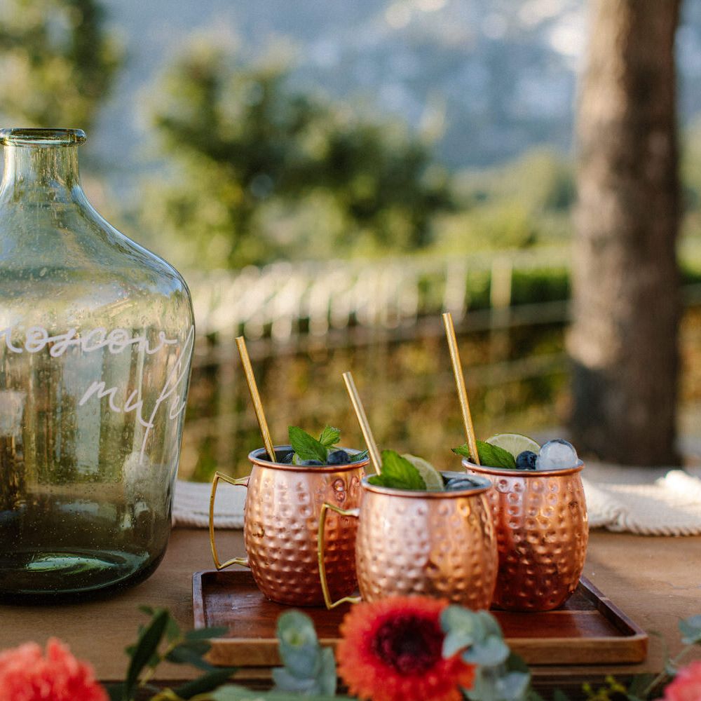 Metal cups filled with cocktails next to large glass vessels with the words 'prosecco' written on them