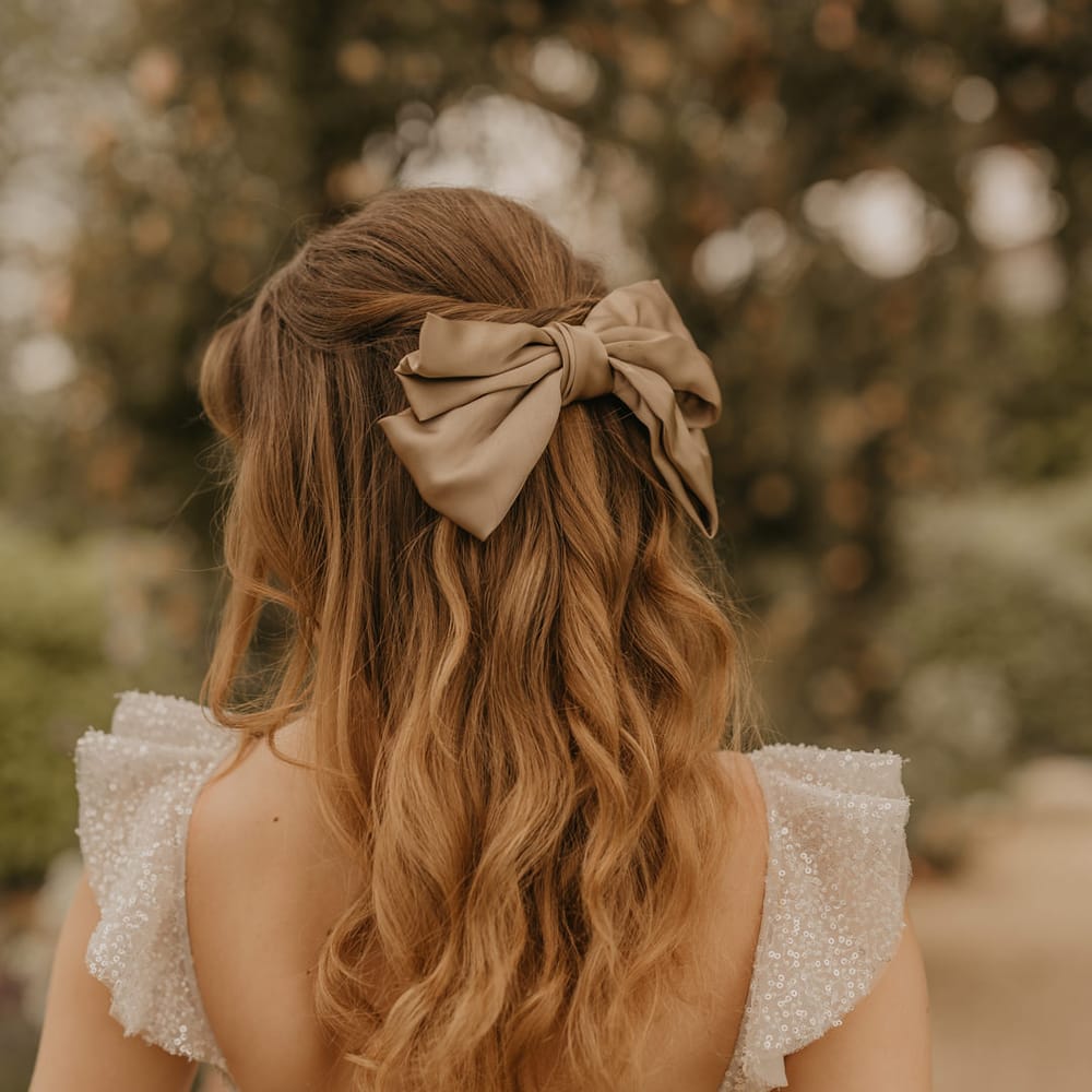 Bride in a sparkly wedding dress with a half up half down wedding hairstyle with satin bow hair accessory 