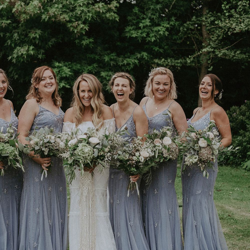 Bride in Grace Loves Lace bardot wedding dress stands in the middle of bridesmaids in blue beaded cami bridesmaid dresses at Isle of Wight wedding with macrame wedding decor