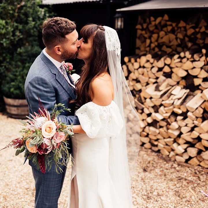 Bride & groom kiss on their wedding day as bride holds floral bouquet