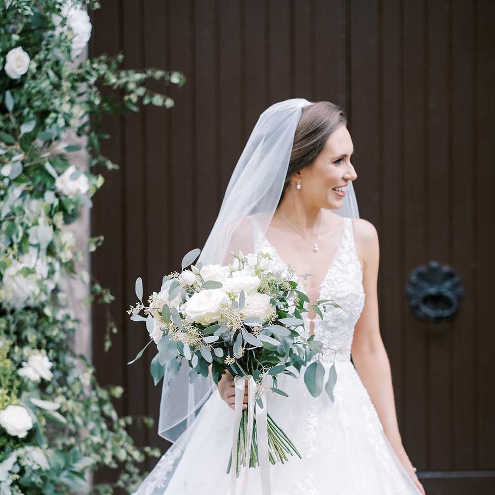 Bride in a Martina Liana Bridal wedding dress and veil holding a white rose and eucalyptus wedding bouquet 