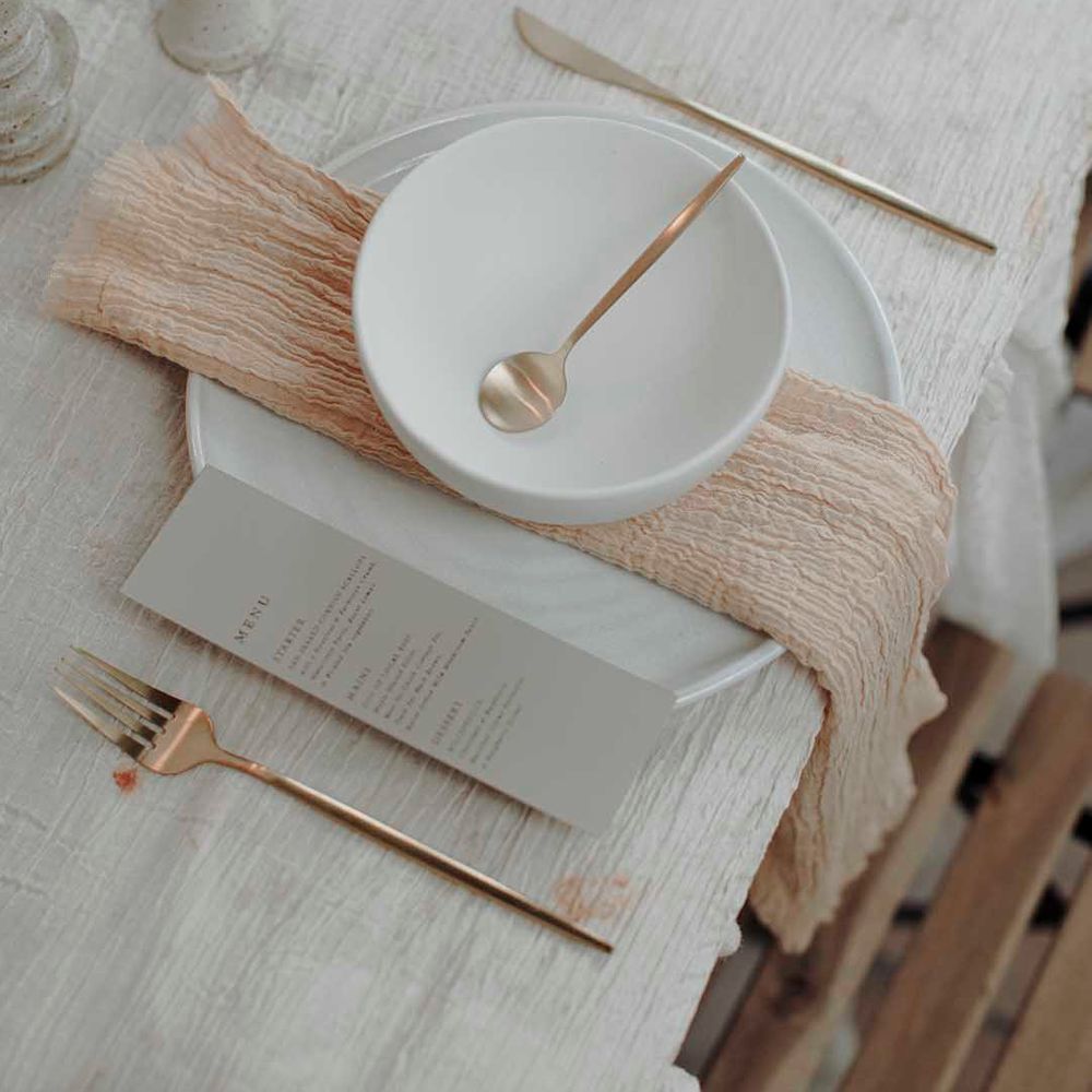 minimalist place setting with charger plate, bowl, linen napkin, menu card and gold cutlery 