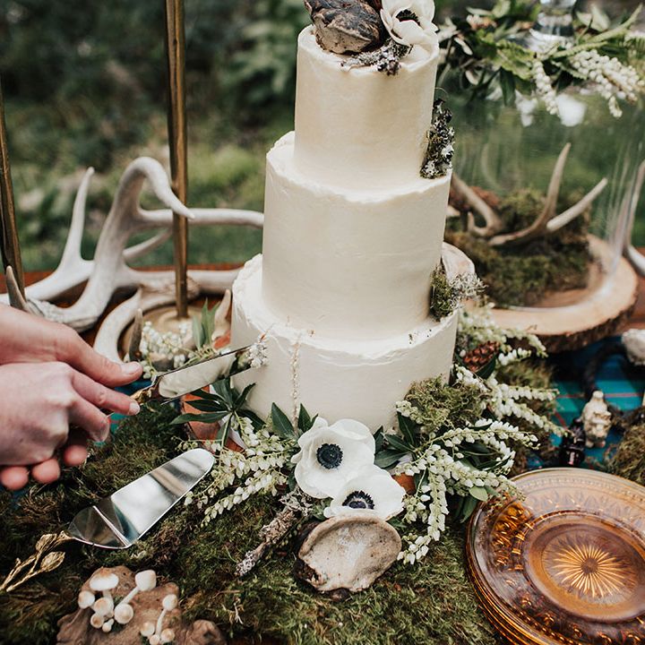 Bride and groom cutting the buttercream wedding cake surrounded by moss and anemone decor 