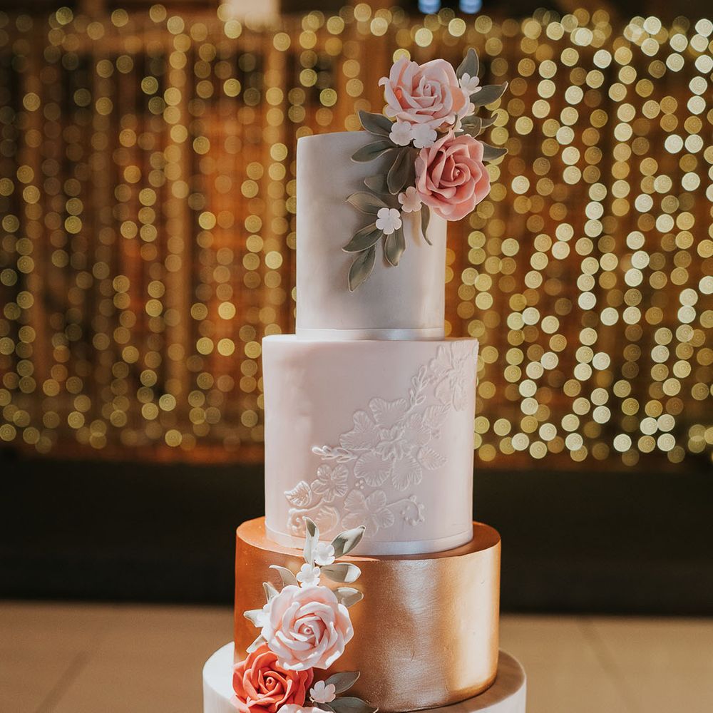 Four tier wedding cake with white frosting and rose gold/copper frosting with decorative roses and details