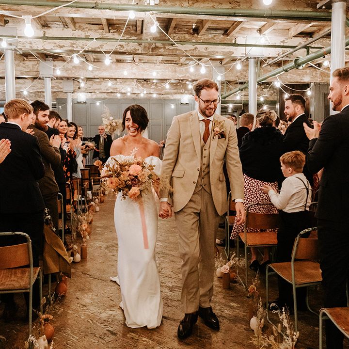 Groom in beige three piece suit and bride in Alexandra Grecco gown walk back down the aisle as a married couple 