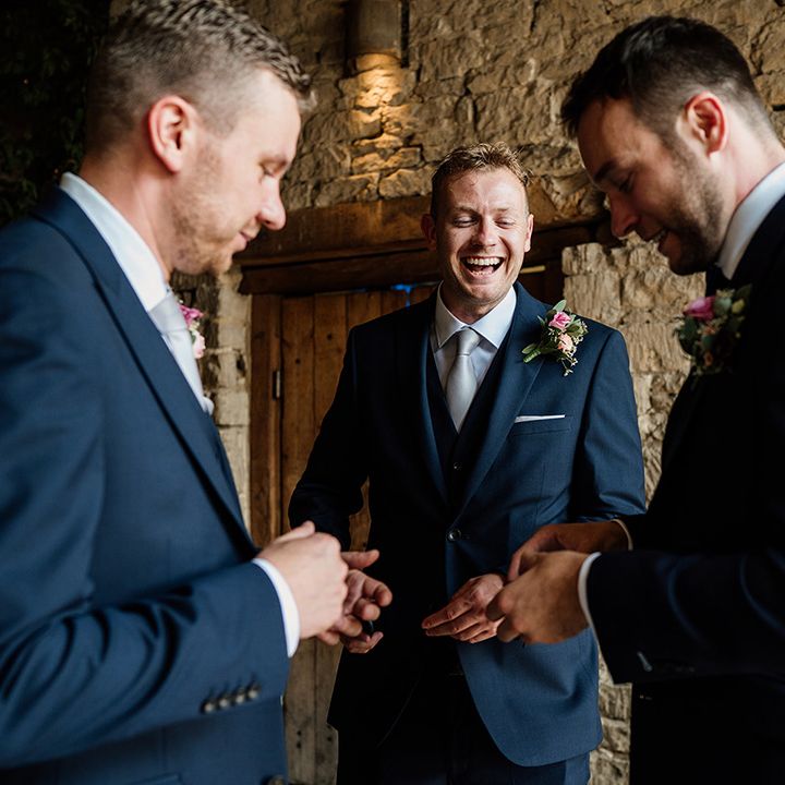 Groom laughs with groomsmen in blue suits and pale blue ties for wedding at Cripps Barn