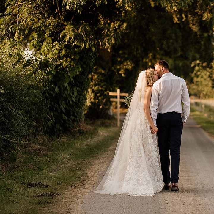 Bride and groom walk along a road holding hands and kissing 