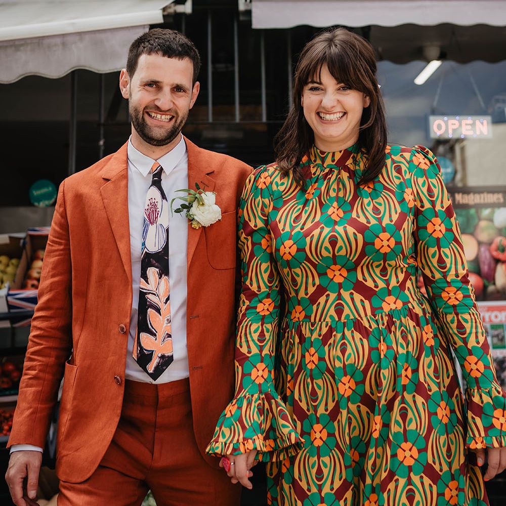 Bride & groom stand beside one another in brightly coloured outfits during wedding reception in Bristol 